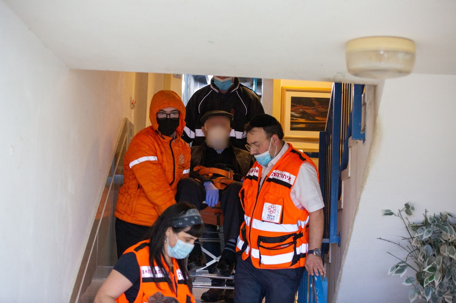 UH volunteers carrying an elderly man down the stairs of his home on the way to receive his vaccine